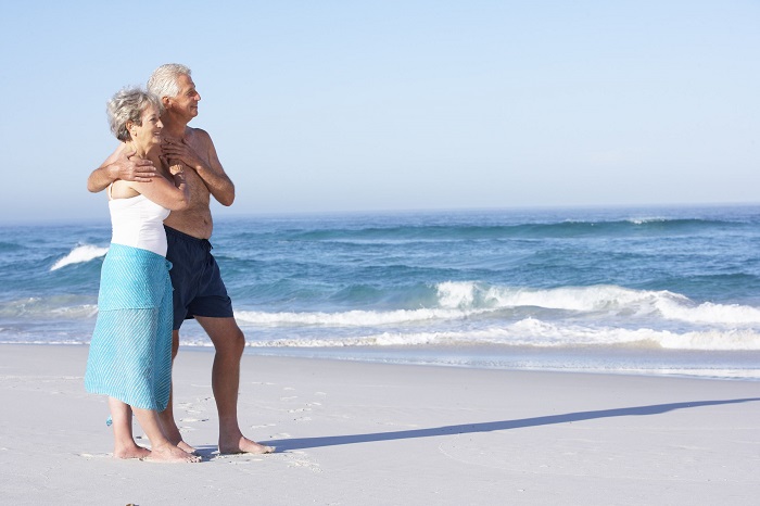 Senior couple on holiday walking along sandy beach