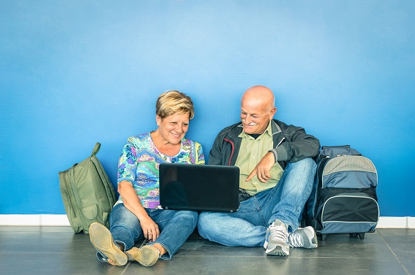 Happy senior couple sitting on the floor with laptop waiting for a flight at the airport