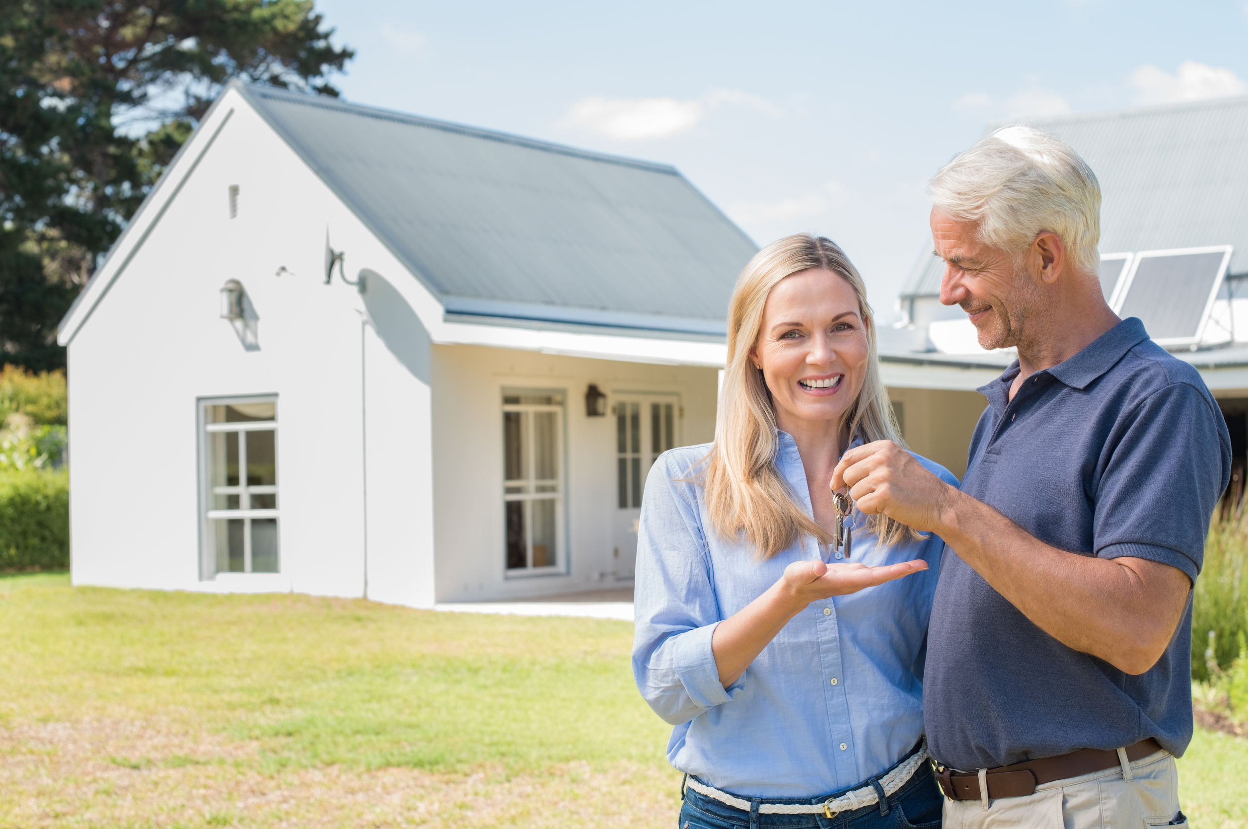Cheerful senior couple standing outside their new house with keys. Retired man giving new house keys to his wife. Senior man and mature woman in the garden of their new house.