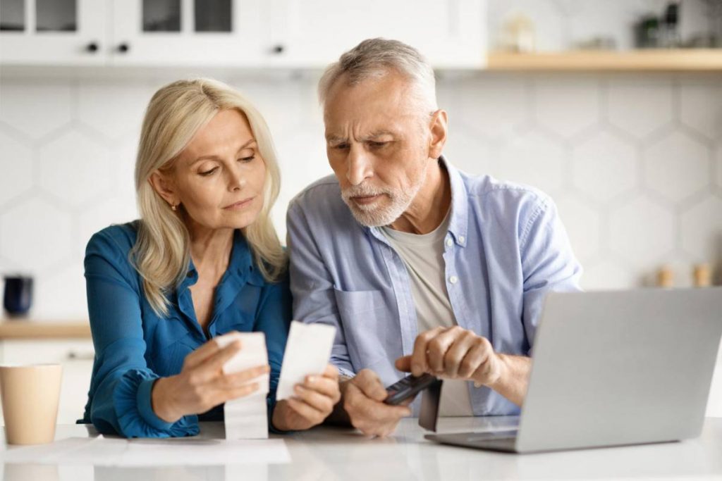 Senior couple in kitchen checking bills and using calculator