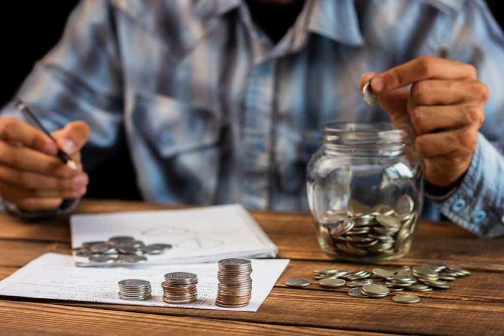 Man counting savings and putting coins in a jar 