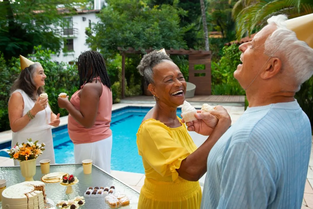 A lively gathering of senior people enjoying a festive party by the poolside, surrounded by vibrant decorations and laughter.