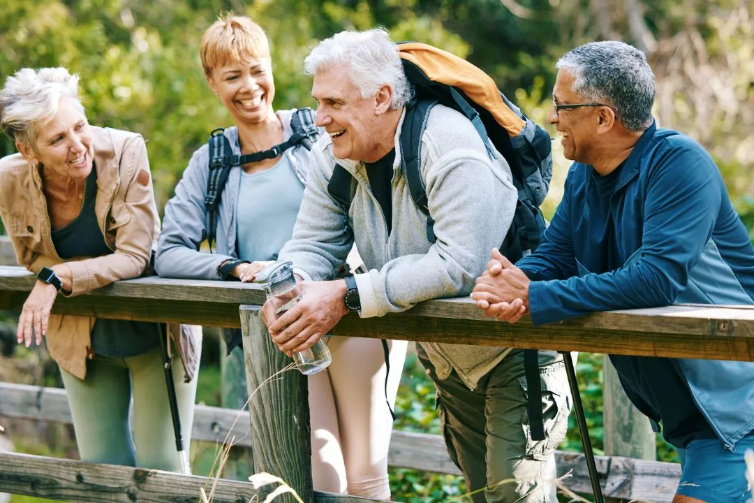 Three older individuals stand on a wooden bridge, enjoying the view and each other's company in a serene outdoor setting.