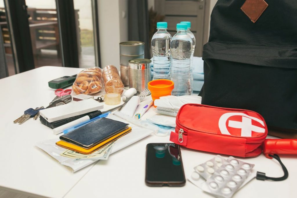 A table featuring a backpack, a cell phone, a water bottle, and assorted items organized on its surface.