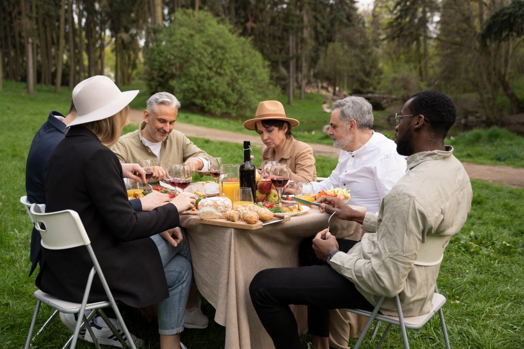 A group of friends laughing and sharing food during a sunny picnic in a lush green park