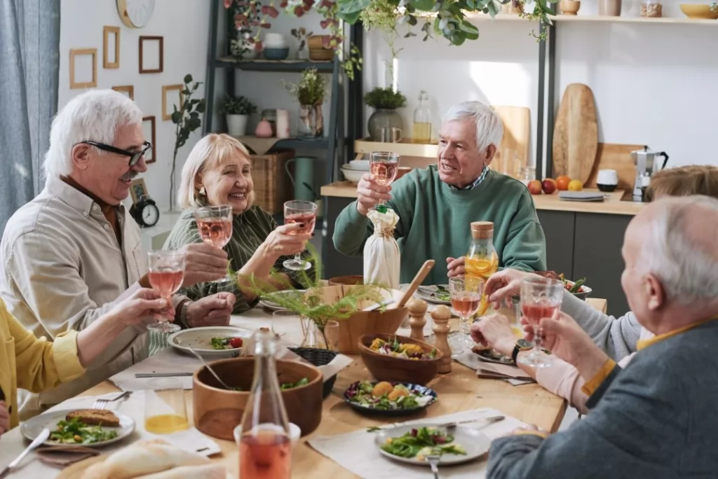 Seniors gathered around a dinner table, laughing and enjoying a meal together in a warm, friendly atmosphere.