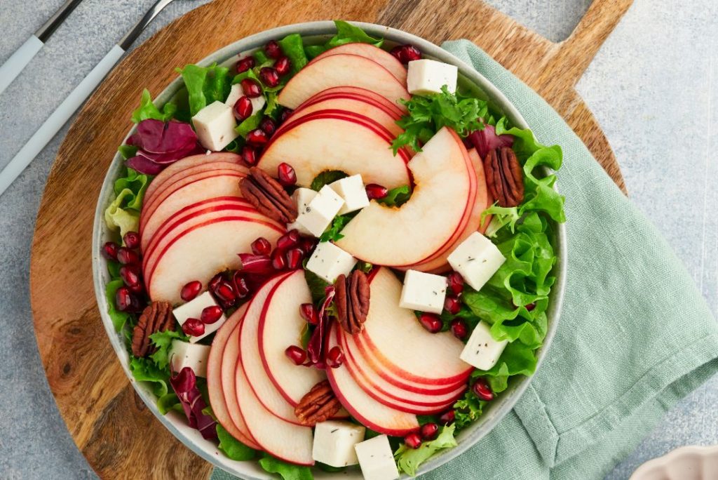 A colorful salad with slices of apples and pears, crumbled feta cheese, and pomegranate seeds, perfect for a nutritious meal.