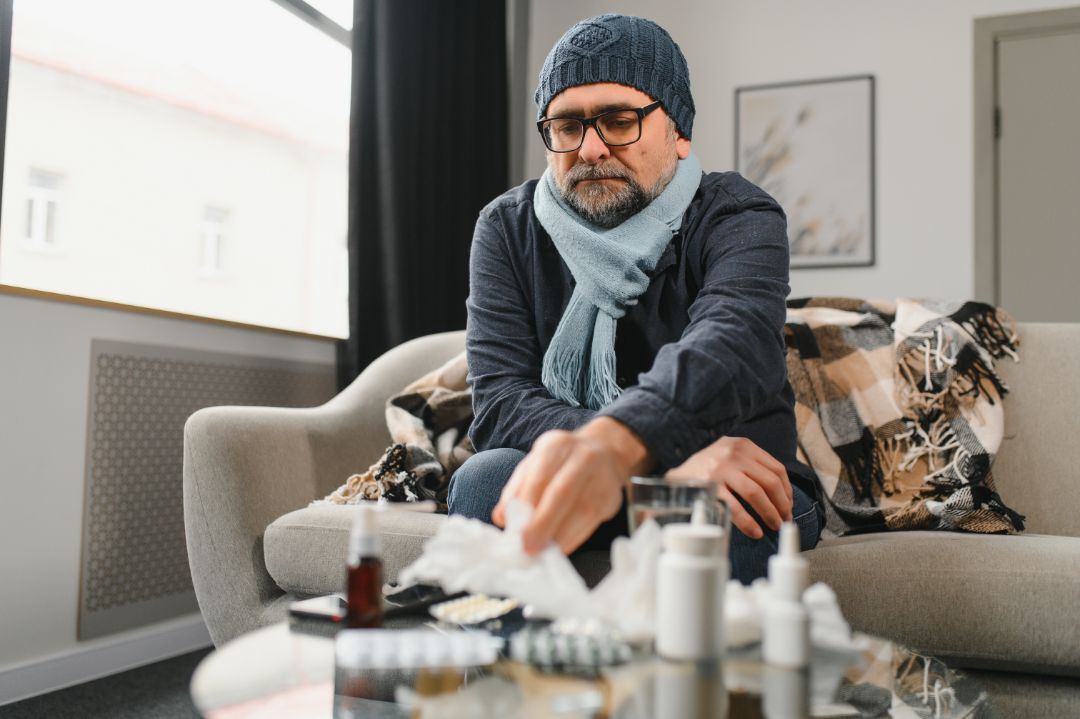 A man seated on a couch, holding a bottle of hand sanitizer, emphasizing personal hygiene in a relaxed setting.