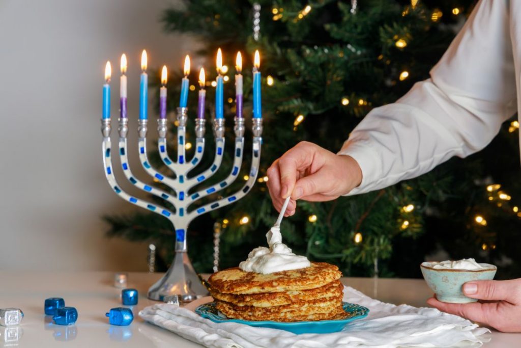 A man holds a plate of pancakes with candles, symbolizing the celebration of Hanukkah at a beautifully arranged table.