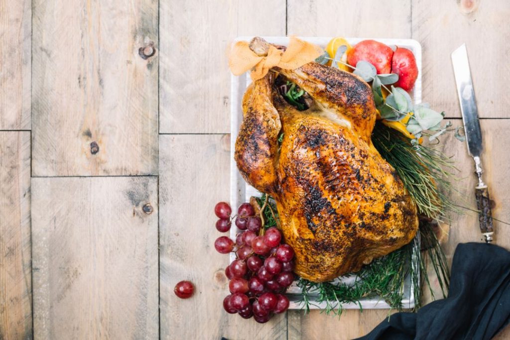 A beautifully roasted turkey on a platter, accompanied by fresh grapes and colorful vegetables, ready for a festive meal.