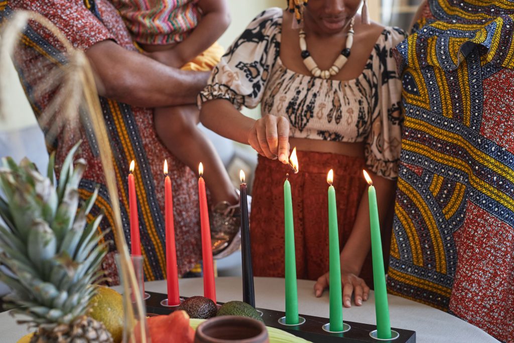 A family gathers around a table, lighting candles in celebration of Kwanzaa, symbolizing unity and tradition.