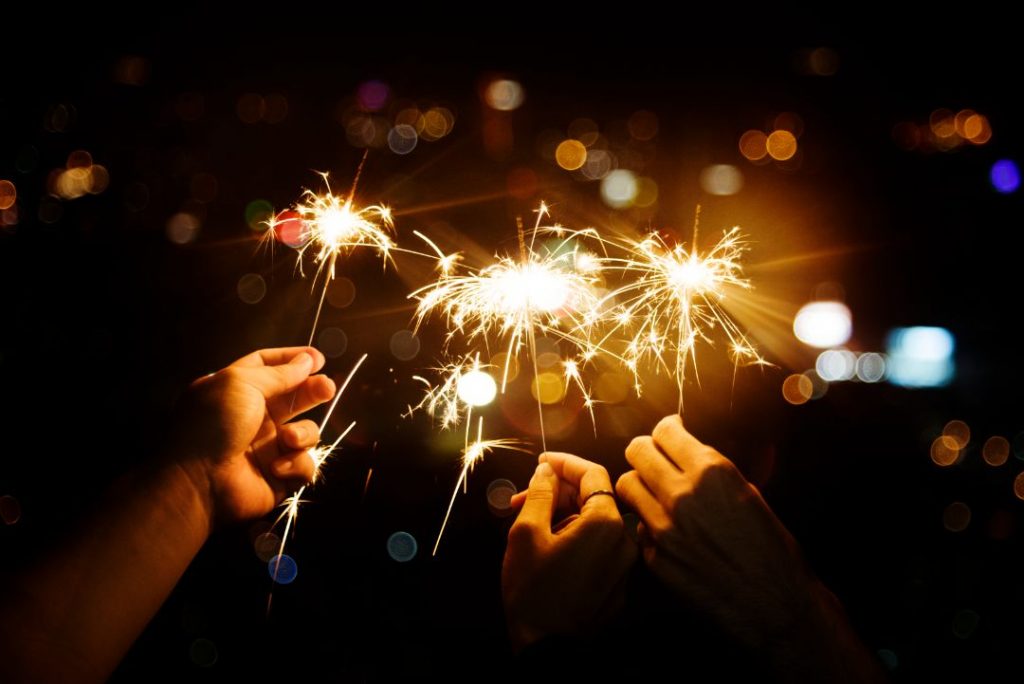 Hands holding sparklers illuminate the darkness, celebrating the New Year with vibrant light and joy.