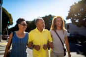 Three individuals, including a man and a woman, walk together on a sunny street, representing the snowbird community.