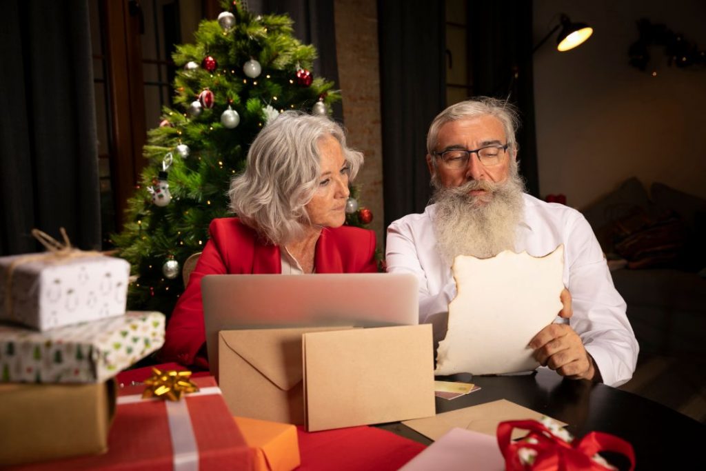 An older couple at a table with a laptop and gifts, reviewing their shopping list together.