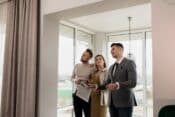 Three individuals look out a window, engaged in discussion about essential home-buying tips and insights.