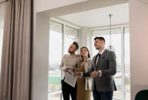 Three individuals look out a window, engaged in discussion about essential home-buying tips and insights.