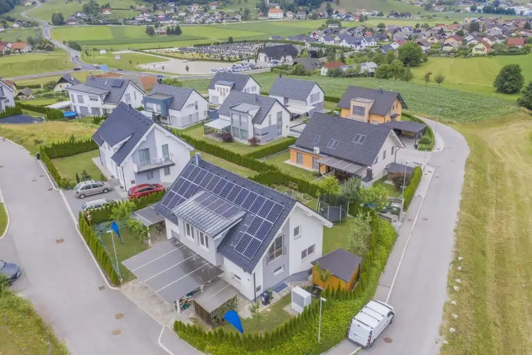 Aerial view of a green eco community neighborhood with modern houses featuring solar panels on the roofs, surrounded by green fields and roads.