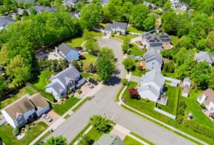 Aerial view of a suburban neighborhood featuring houses, streets, and green spaces under a clear blue sky.