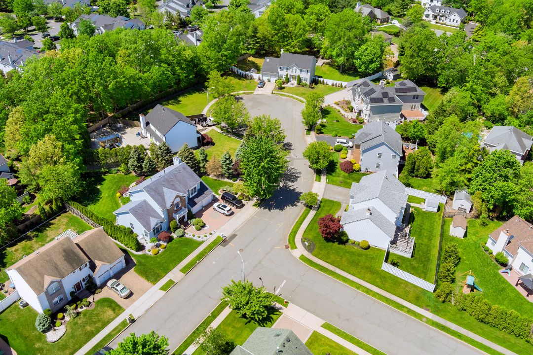 Aerial view of a suburban neighborhood featuring houses, streets, and green spaces under a clear blue sky.