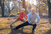A senior couple performing yoga exercises in a vibrant park, with lush grass and trees in the background.