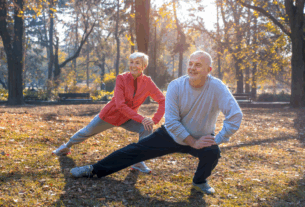 A senior couple performing yoga exercises in a vibrant park, with lush grass and trees in the background.