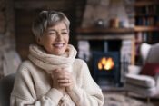 1. A woman wearing a sweater and scarf sits comfortably in front of a glowing fireplace, enjoying the warm ambiance.