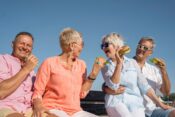 2. A group of four seniors sharing hamburgers together on a park bench, smiling and engaged in conversation.
