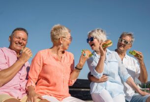 2. A group of four seniors sharing hamburgers together on a park bench, smiling and engaged in conversation.