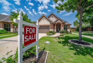 1. A for sale sign stands in front of a suburban home, indicating the property is available for purchase.